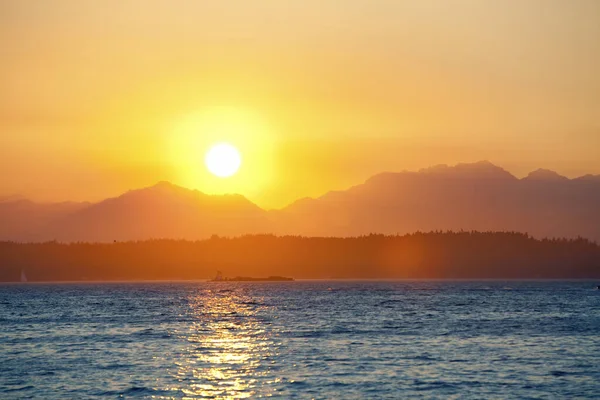 Pôr-do-sol laranja atrás de montanhas com lago em primeiro plano — Fotografia de Stock