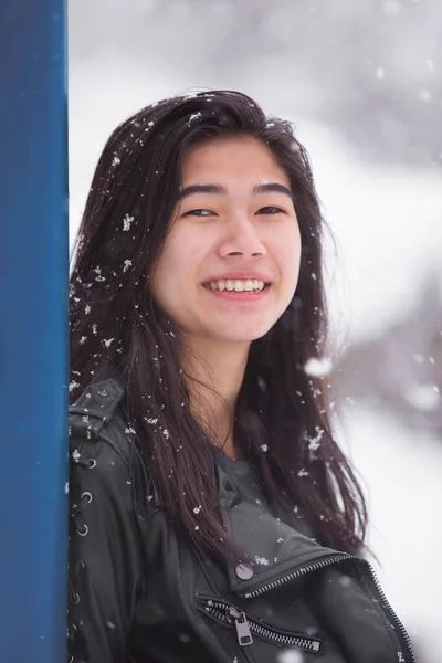 Asian teen girl leaning against post  outdoors in snowfall smili — Stok fotoğraf