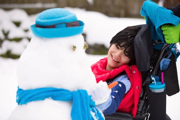 Szczęśliwy uśmiechający się wyłączone chłopak na wózku inwalidzkim, budowa snowman — Zdjęcie stockowe