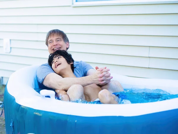 Padre seduto nella vasca idromassaggio con figlio disabile all'aperto ridendo — Foto Stock