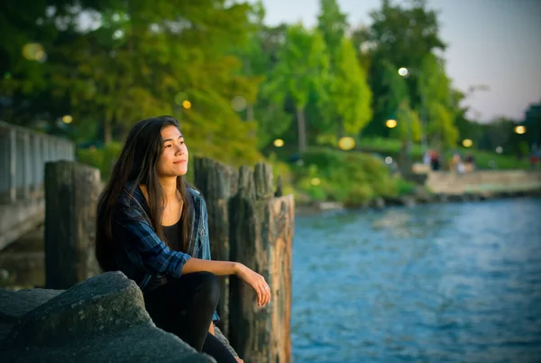 Biracial adolescente menina sentada olhando para fora sobre lago ao pôr do sol — Fotografia de Stock