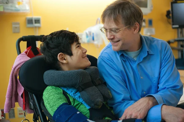 Padre hablando con hijo discapacitado en silla de ruedas en la sala de espera —  Fotos de Stock