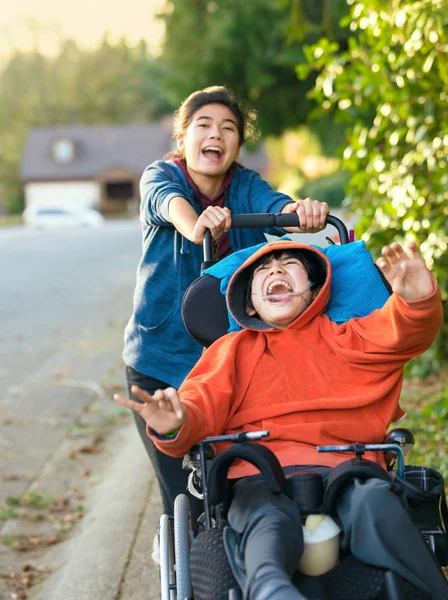 Teen girl pushing disabled boy in wheelchair outdoors, laughing — Stock Photo, Image