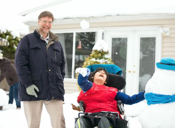 Far med handikappad son i rullstol leker med snöbollar — Stockfoto