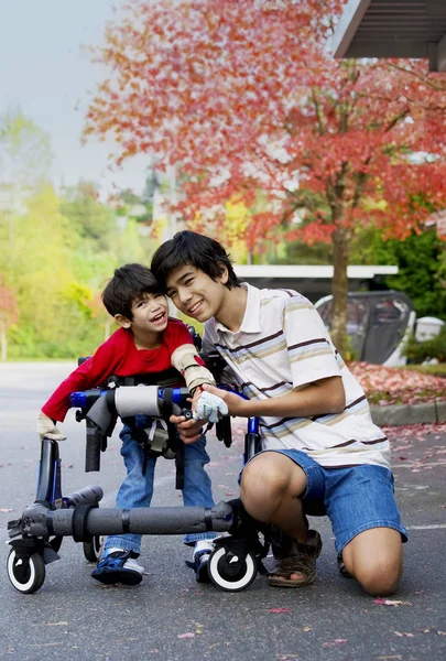 Fratello maggiore aiutare piccolo disabile ragazzo camminare in walker all'aperto — Foto Stock