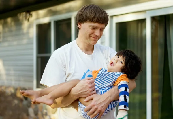 Ojciec trzyma niepełnosprawnego syna w ramionach poza domem. — Zdjęcie stockowe