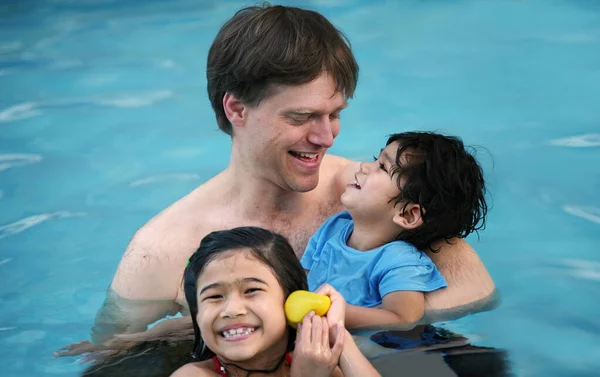 Pai caucasiano na piscina com crianças biraciais, segurando incapacitante — Fotografia de Stock