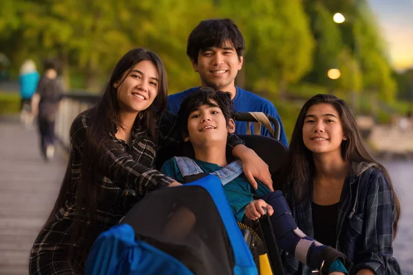 Brother and sisters surrounding disabled boy in wheelchair at pa — ストック写真