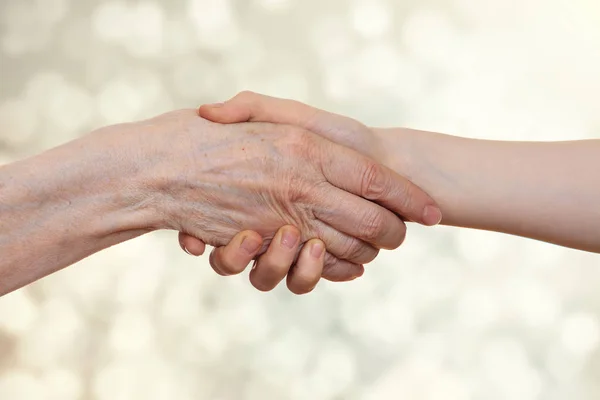 Handdruk tussen een oude persoon met een gerimpelde hand en een jongen, op een lichte achtergrond van beige bokeh. — Stockfoto