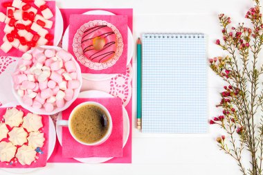 Fincan kahve, çörek, lezzetli aperatifler, defter, kalem ve çiçekler