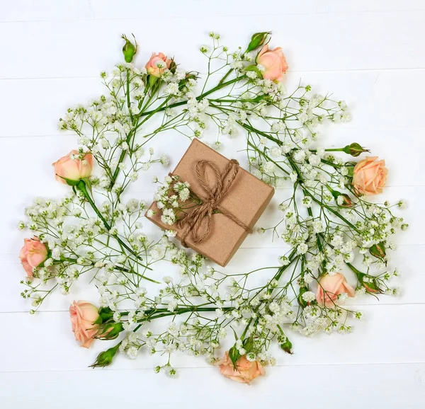 Fleurs avec une boîte cadeau sur une table en bois blanc, style plat — Photo