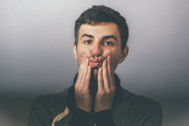 Genç adam elleriyle yanaklarını sıkıyor.