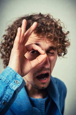 Elleri gözlerinde, parmaklarından bakan komik bir adam.