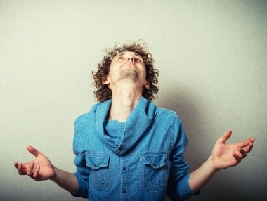 Kıvırcık saçlı adam dua ediyor ve gökyüzüne bakıyor.