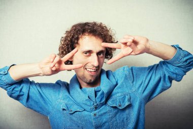 Kıvırcık saçlı adam iki parmağını gösteriyor.