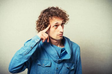 Şakağına parmağını uzatan kıvırcık saçlı bir adam.