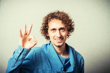Kıvırcık genç adam iyi bir jest yapıyor. Gri bir arkaplanda