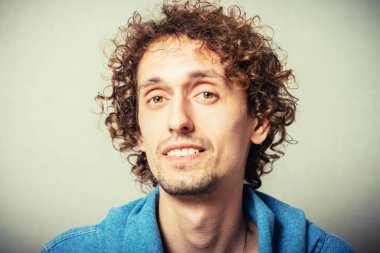 Kıvırcık genç adam dişçiden sonra dişlerini göstererek gülüyor. Gri bir arkaplanda