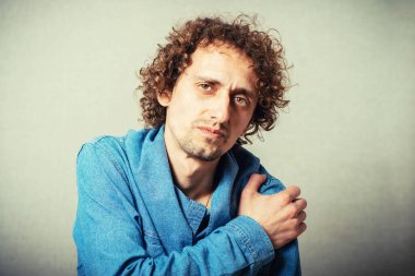 Omzum ağrıyan kıvırcık genç adam. Gri bir arkaplanda