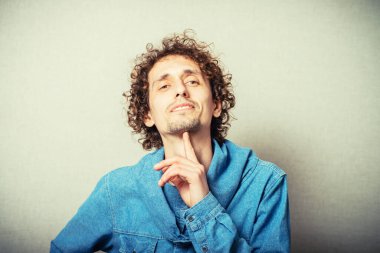 Kıvırcık genç adam kameraya bakıp başını eline koydu. Gri bir arkaplanda