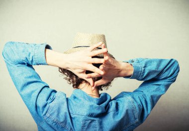 Hasır şapkalı kıvırcık genç adam ellerini dinlendiriyordu. Arkadan bak. Gri bir arkaplanda