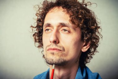 Kıvırcık genç bir şey planlıyor, kalemle not alıyor. Gri bir arkaplanda