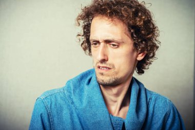 Kıvırcık genç erkek kırgınlığı ve kötü ruh hali. Gri bir arkaplanda