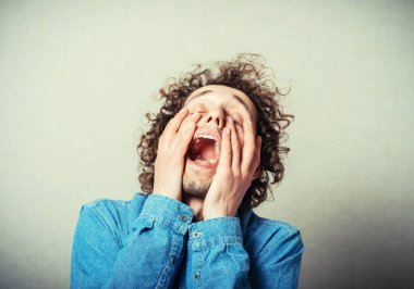 Kıvırcık genç adam ağlıyor, elleri suratında bağırıyor. Gri bir arkaplanda