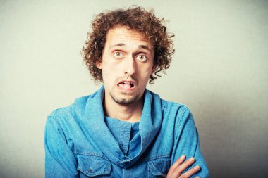 Kıvırcık saçlı adam sürpriz bir şekilde ağzını açtı. Gri bir arkaplanda.