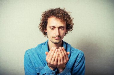Kıvırcık saçlı adam avuç içi jestine boş bakar. Gri bir arkaplanda.