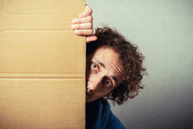 Boş kartonu olan kıvırcık adam. Gri bir arkaplanda.