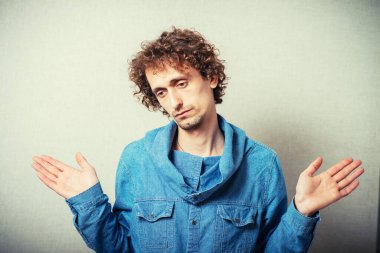 Kıvırcık adam jest yapıyor. Elimde hiçbir şey yok. Ellerim boş. Gri bir arkaplanda.