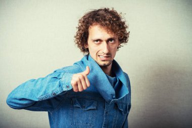 Kıvırcık adam baş parmağını kaldırıyor. Tamam, güzel, güzel, harika. Gri bir arkaplanda.