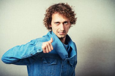 Kıvırcık adam baş parmağını kaldırıyor. Tamam, güzel, güzel, harika. Gri bir arkaplanda.