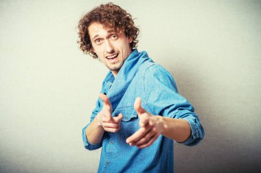 Kıvırcık adam işaret parmağı kameraya doğru. Gri bir arkaplanda.