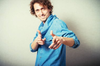 Kıvırcık adam işaret parmağı kameraya doğru. Gri bir arkaplanda.