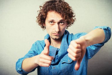 Kıvırcık adam işaret parmağını kameraya doğru tutar ve kötü bir hareket yapar. Gri bir arkaplanda.