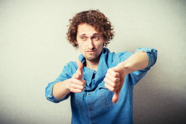 Kıvırcık adam işaret parmağını kameraya doğru tutar ve kötü bir hareket yapar. Gri bir arkaplanda.