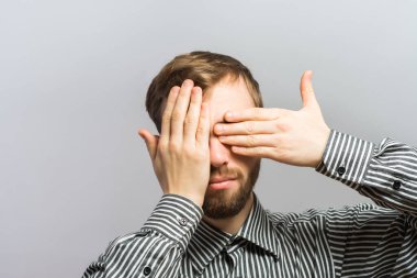 Genç yakışıklı adam elleriyle gözlerini kapattı. Jest yap. Gri bir arkaplanda