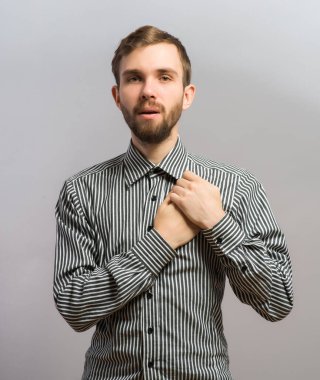 Genç ve yakışıklı bir adam üzgün, kalbini ve kalbini koruyor. Jest yap. Gri bir arkaplanda