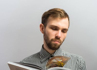 Kitap okuyan genç yakışıklı bir adam. Jest yap. Gri bir arkaplanda