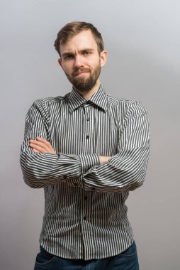 Gri arka planda poz veren mutsuz genç adamın portresi. Yakışıklı genç İspanyol erkek model. Kollarını kavuşturup kameraya bakıyor..