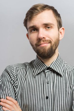 Gri arka planda poz veren genç bir adamın portresi. Yakışıklı genç İspanyol erkek model. Kollarını kavuşturup kameraya bakıyor..