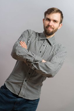 Gri arka planda poz veren mutsuz genç adamın portresi. Yakışıklı genç İspanyol erkek model. Kollarını kavuşturup kameraya bakıyor..