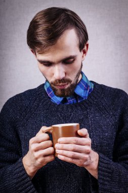 Sakallı genç erkek, bir fincan çay üflüyor.