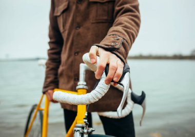 Elleri gölün yanında bisikletin direksiyonunda olan genç bir adam.