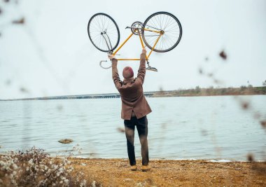 Genç bir adam bisikletini gölün yanında kaldırdı.