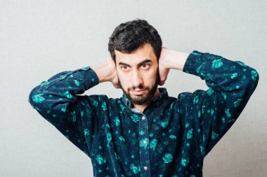 Tişörtlü, sakallı, genç bir adamın yakından çekilmiş portresi. Komşulara bakarak gürültüyü engellemek için el ele tutuşmuş.