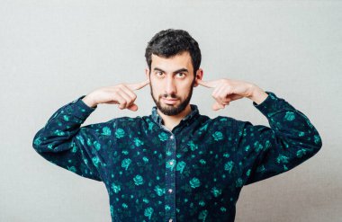 Tişörtlü, sakallı, genç bir adamın yakından çekilmiş portresi. Komşulara bakarak gürültüyü engellemek için el ele tutuşmuş.