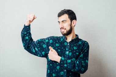 Zirveye ulaştım! Gri arka planda dururken gülümseyen mutlu genç adam.